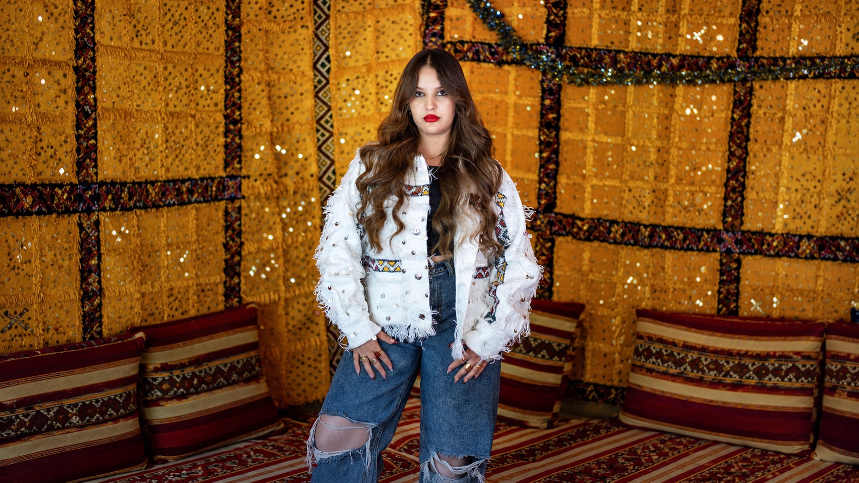 Model in a white sequined jacket standing in a golden Moroccan textile tent