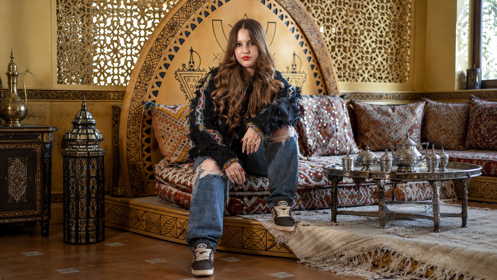 Model in a fringed black jacket and ripped jeans seated in a Moroccan tea room